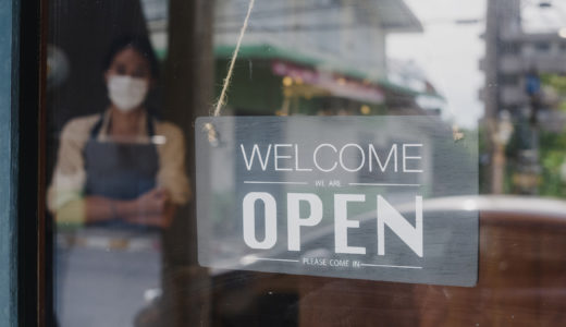 Retail working in a mask standing behind an open sign
